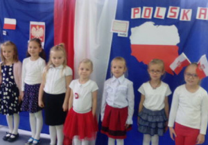 Grupka dziewczynek pozuje do zdjęcia na tle patriotycznej dekoracji.